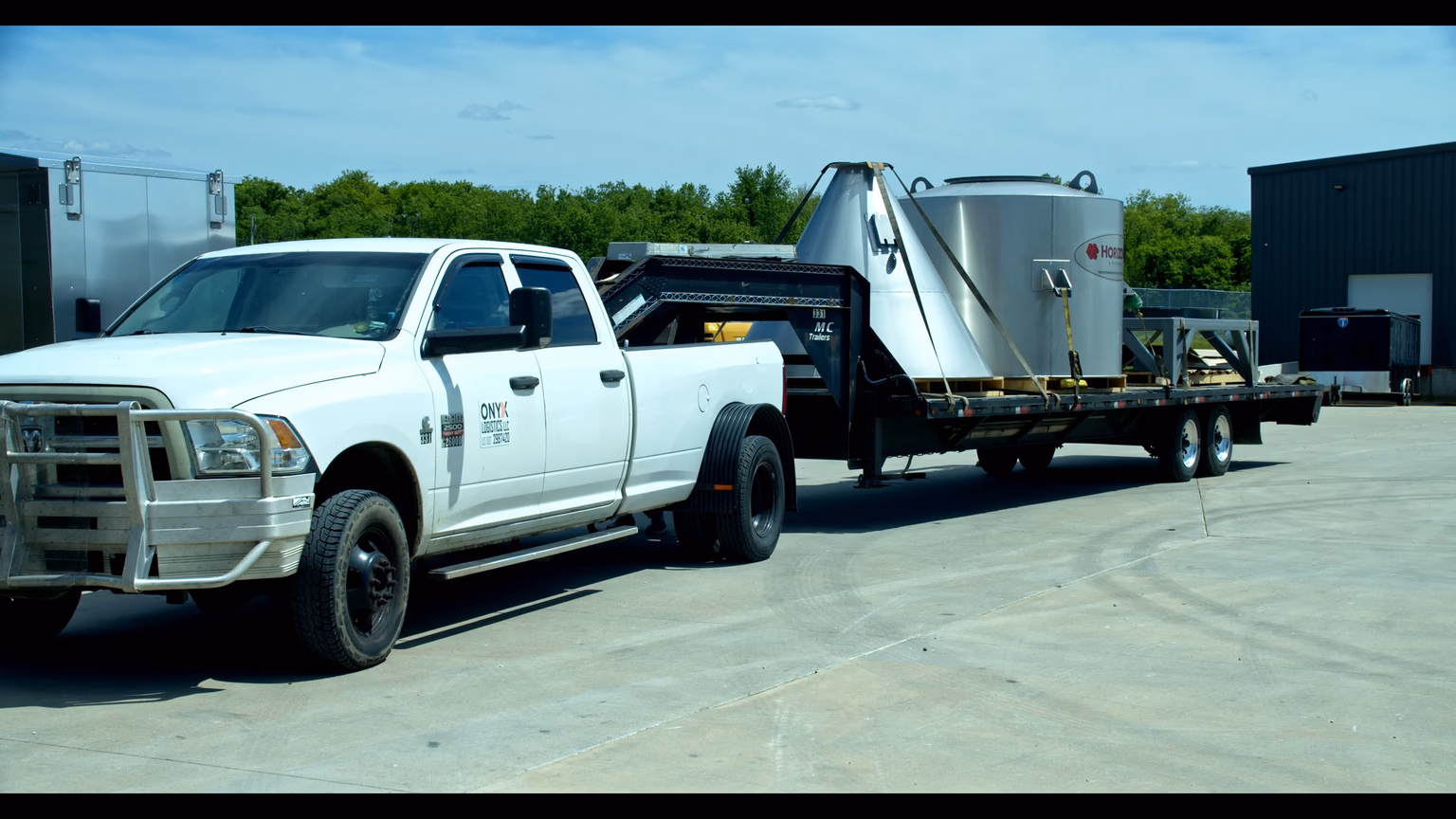 An Onyx Logistics Ram 2500 HD with a heavy-duty grille guard, hooked to a gooseneck flatbed loaded with a Horizon Systems silver tank, parked on a concrete yard at the Strafford, Missouri facility.