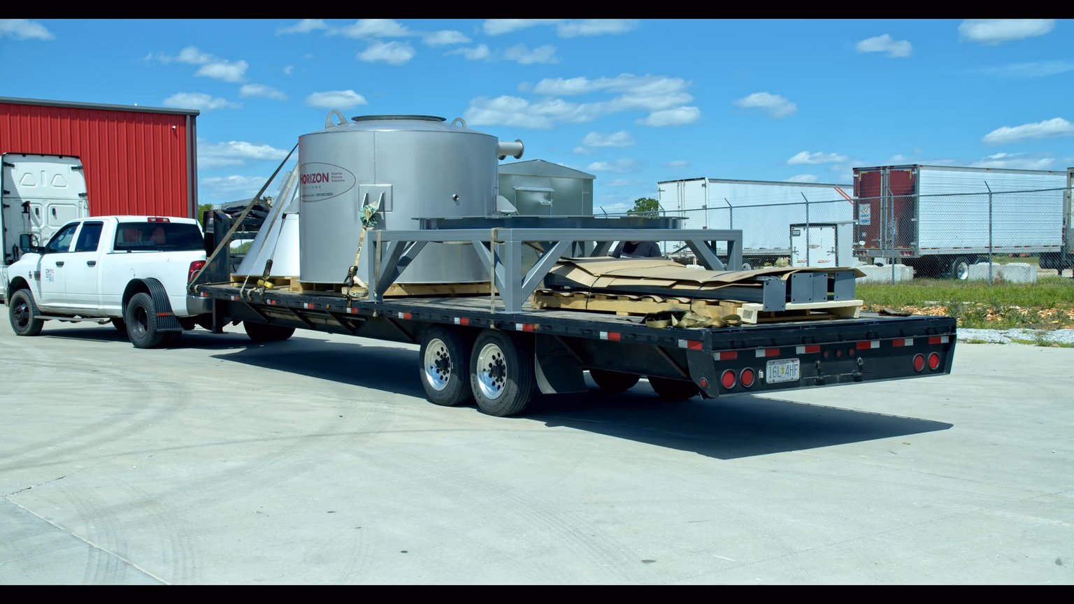 Rear three-quarter view of an Onyx Logistics gooseneck flatbed loaded with a Horizon Systems silver tank and steel framing, parked at the Strafford, Missouri yard.